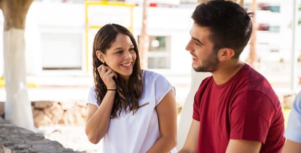 Photo of a girl touching her neck while talking to a guy