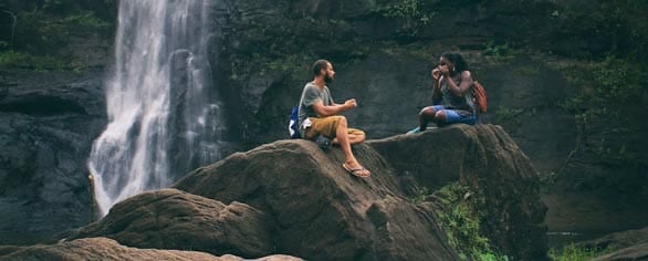 Screenshot of two people talking by a waterfall