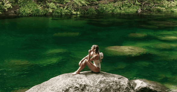 girl sitting on rock by river