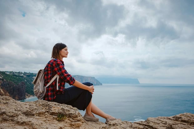 woman traveling with backpack tourist on seashore in summer. Enjoying Beautiful clouds sky among Mighty Cliffs Meeting Ocean. the idea and concept of freedom, vacation and discovery