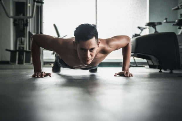 Muscular bodybuilder guy doing push ups in gym.