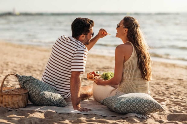leisure, relationships and people concept - happy couple with food eating and having picnic on beach