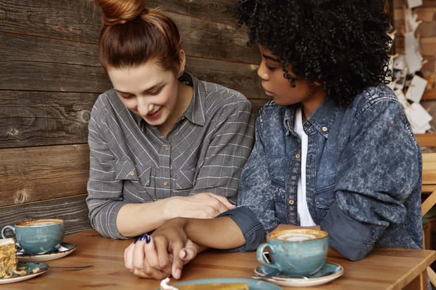 Candid shot of beautiful interracial homosexual female couple spending nice time together, sitting at cafe table with mugs and dessert, sharing sweet moment of their love. People and relationships Candid shot of beautiful interracial homosexual female couple spending nice time together, sitting at cafe table with mugs and dessert, sharing sweet moment of their love. People and relationships