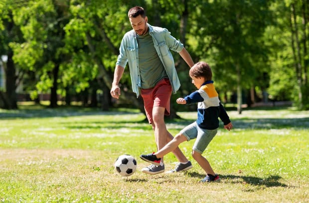 family, fatherhood and people concept - happy father and little son with ball playing soccer at summer park