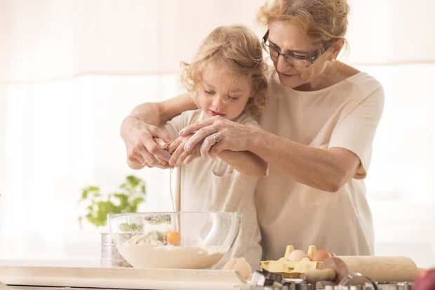 Senior nanny helping child to break the egg into a bowl Senior nanny helping child to break the egg into a bowl