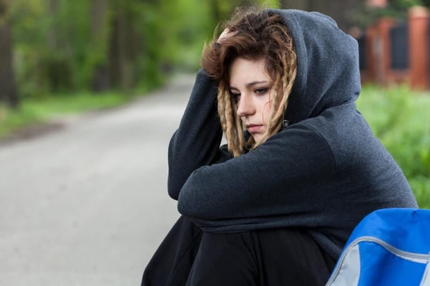 Depressed young girl in hood sitting down on road