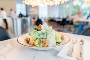 Caesar salad in bowl next to fork and knife in airy and light restaurant