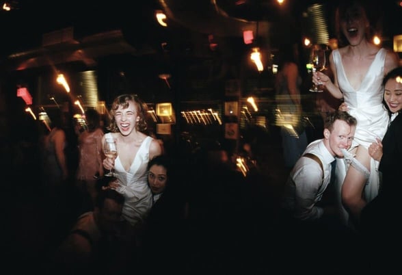 woman wearing wedding dress being hoisted while man grips garter with his teeth