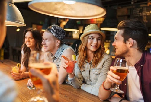 people, leisure, friendship and communication concept - group of happy smiling friends drinking beer and cocktails talking at bar or pub