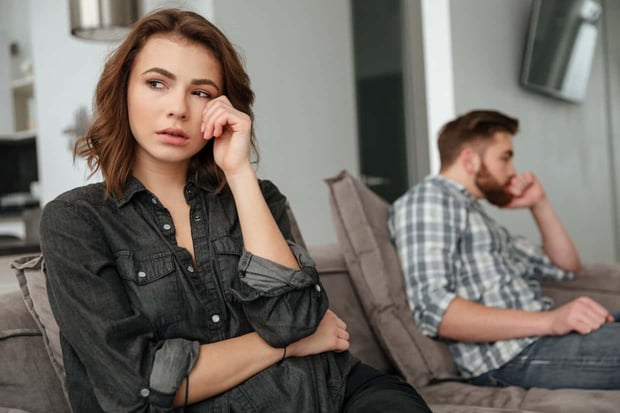 Photo of young sad quarrel loving couple sitting on sofa indoors Looking aside