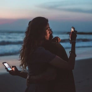 couple embracing on the beach looking at their cellphones