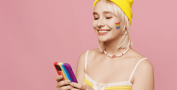 Blonde young woman with rainbow flag face tattoo holding smartphone
