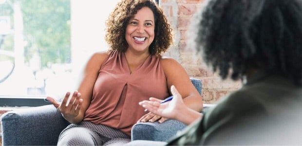 Smiling woman on couch speaking to therapist, slightly off camera. Smiling woman on couch speaking to therapist, slightly off camera.