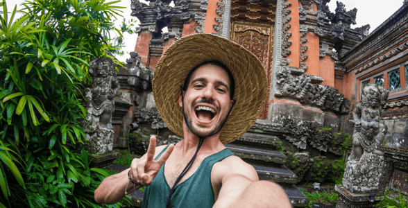 Man taking a peace sign selfie in front of a temple