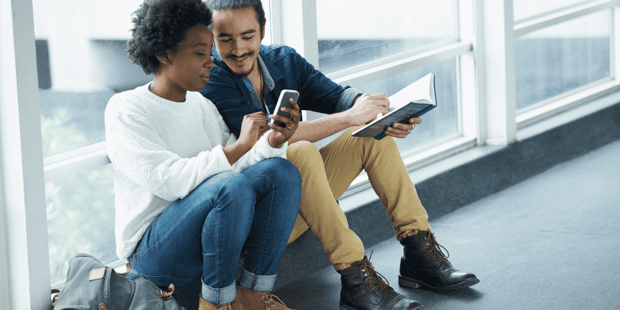 Interracial college couple sitting together looking at a smartphone