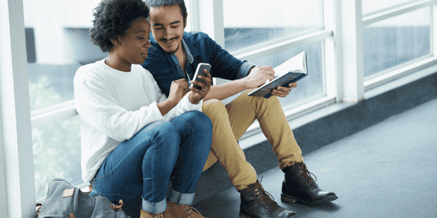 Interracial college couple sitting together looking at a smartphone Interracial college couple sitting together looking at a smartphone