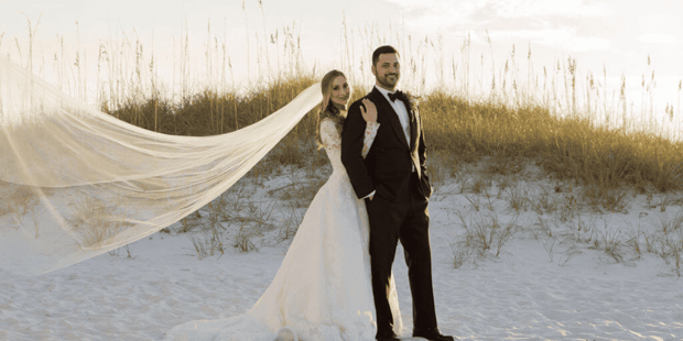 Bride and groom on beach with veil flowing in the wind