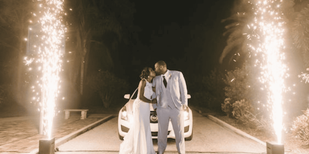 Newly married couple in front of a white car in between pyrotechnics 