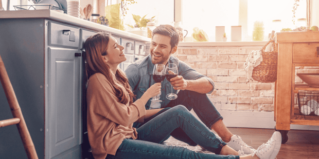Woman and man couple sitting on kitchen floor clinking wine glasses 
