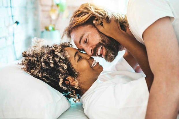 Interracial couple laying on bed laughing and kissing
