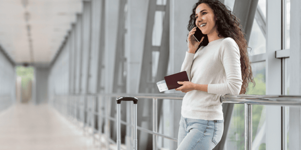 Young woman with long curly hair holing a passport and talking on the phone in an airport
