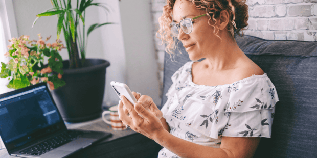 Middle aged woman with curly hair sitting on a couch and scrolling on her cellphone
