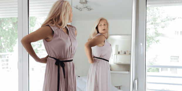 Older blonde woman getting dressed in front of a full length mirror