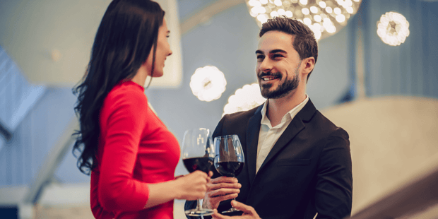 Beautiful woman with dark hair in a red dress talking with handsome man in a black suit, both holding glasses of wine Beautiful woman with dark hair in a red dress talking with handsome man in a black suit, both holding glasses of wine