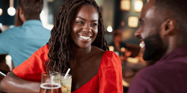 Black woman and Black man wearing red and sitting at a bar counter and laughing