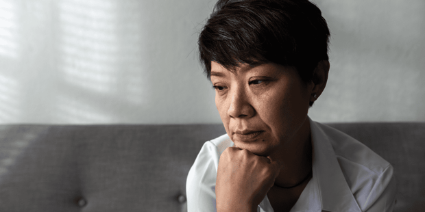 Middle aged Asian woman sitting on couch upset