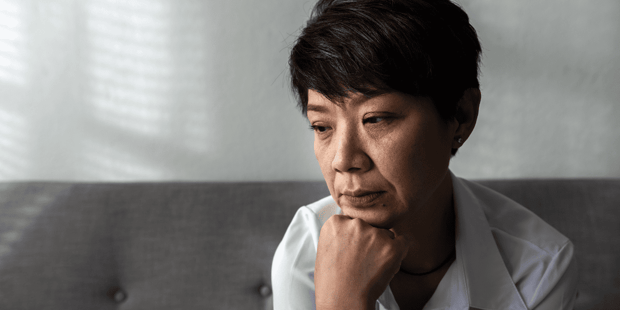 Middle aged Asian woman sitting on couch upset Middle aged Asian woman sitting on couch upset