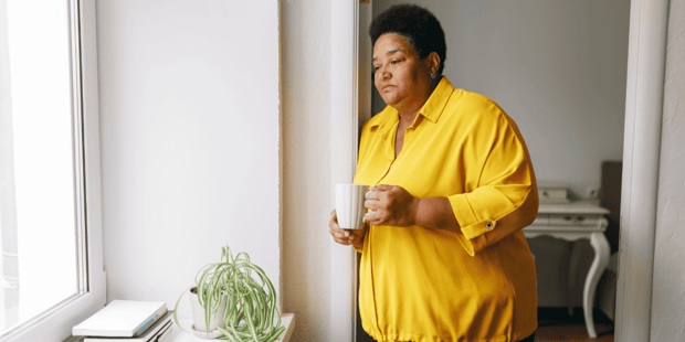 Older Black woman wearing yellow top sad looking out a window Older Black woman wearing yellow top sad looking out a window