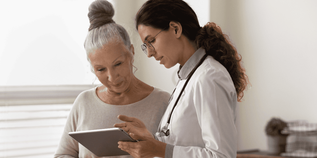 Older woman with hair in a bun talking to young woman doctor about information on a tablet