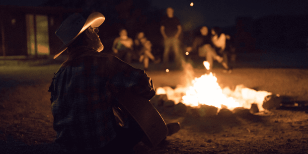 Cowboy sitting in front of a bonfire playing a guitar and singing at Sandy Valley Ranch