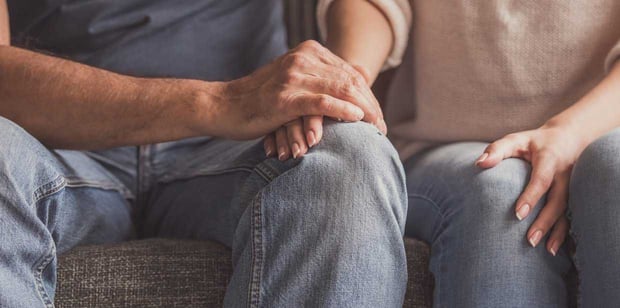 Close-up photo of a couple holding hands while sitting on a sofa. Close-up photo of a couple holding hands while sitting on a sofa.