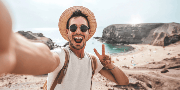 Young man in hat and sunglasses taking peace sign selfie while traveling