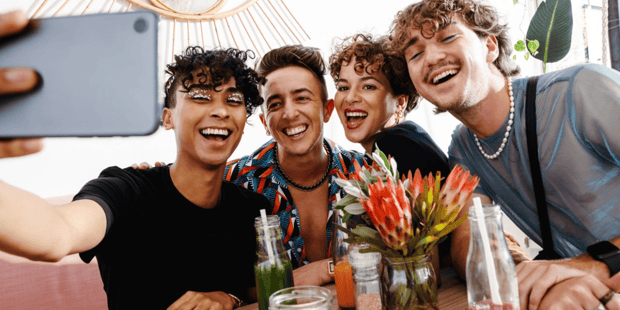 Group of queer friends smiling in a restaurant and taking a selfie Group of queer friends smiling in a restaurant and taking a selfie