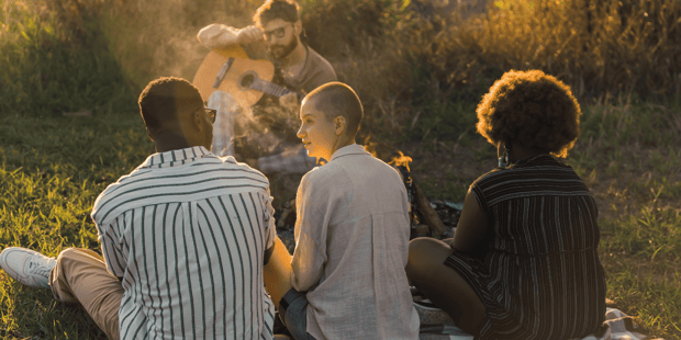 Diverse group of friends at a picnic with one playing guitar Diverse group of friends at a picnic with one playing guitar