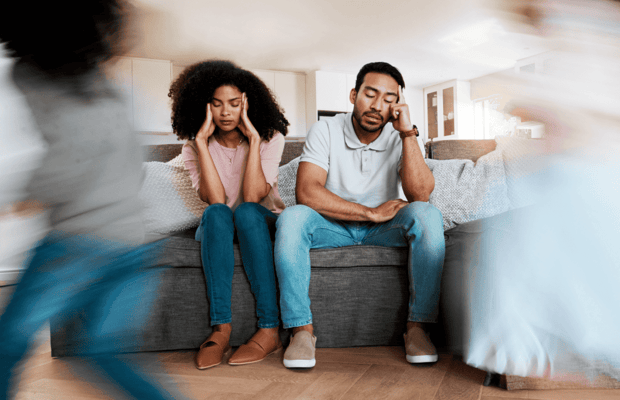 Photo of stressed couple at home with kids running around