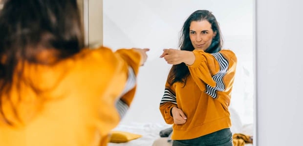 Photo of a woman pointing at herself in the mirror and smiling.