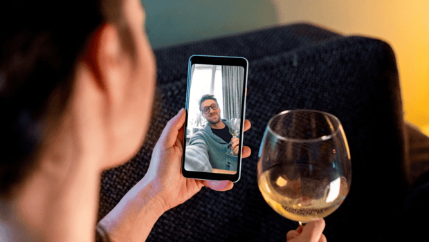 A woman on a video call with a man holding a glass of wine