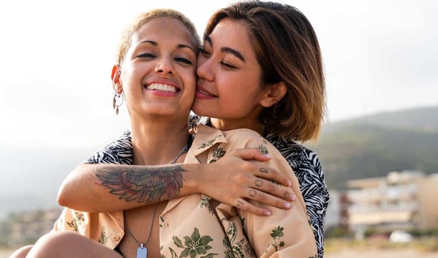 Two womxn cuddling together outside and smiling