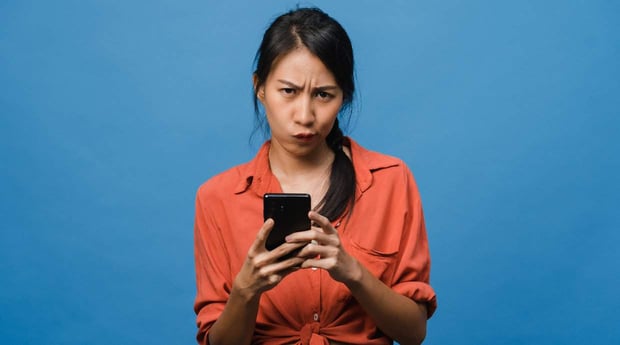 Women in orange shirt scowling at phone