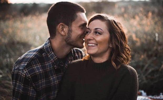 Photo of a man and woman laughing and cuddling in a field
