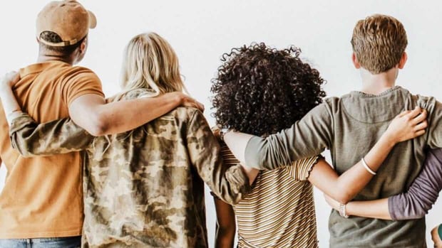 Photo of four people with their arms around each other from behind