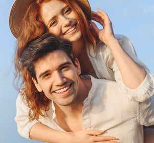 Photo of a young couple piggy back ride woman wearing a hat