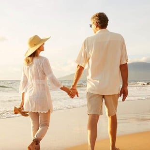 Photo of older couple holding hands and walking on beach