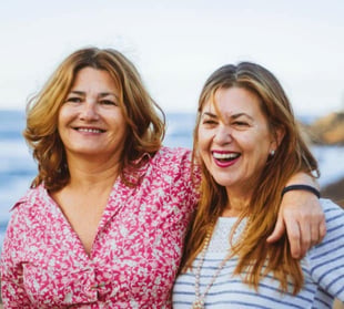 Photo of two women friends standing and smiling with their arms around each other Photo of two women friends standing and smiling with their arms around each other