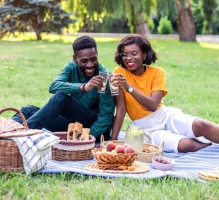 Photo of a young Black couple having a picnic together and smiling and clinking glasses together Photo of a young Black couple having a picnic together and smiling and clinking glasses together