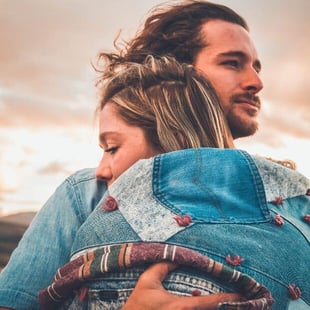 Stock photo of a young white couple hugging while the man looks seriously over the woman's shoulder